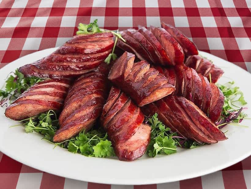 Grilled sausages sliced on a white plate garnished with fresh greens, showcasing Sebi's Kitchen catering for weddings and events.